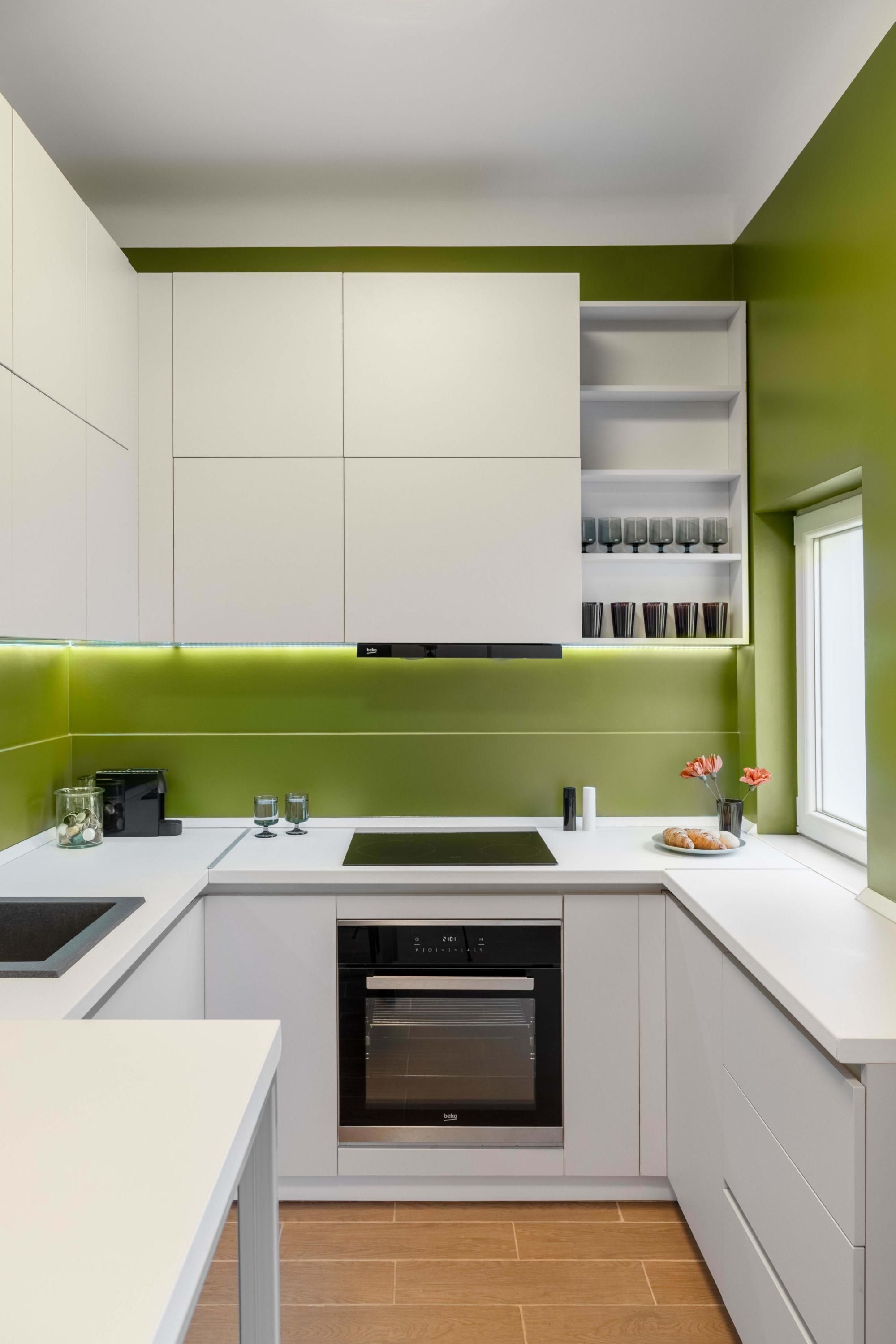 A modern kitchen with white cabinets, a built-in oven, and a green accent wall.