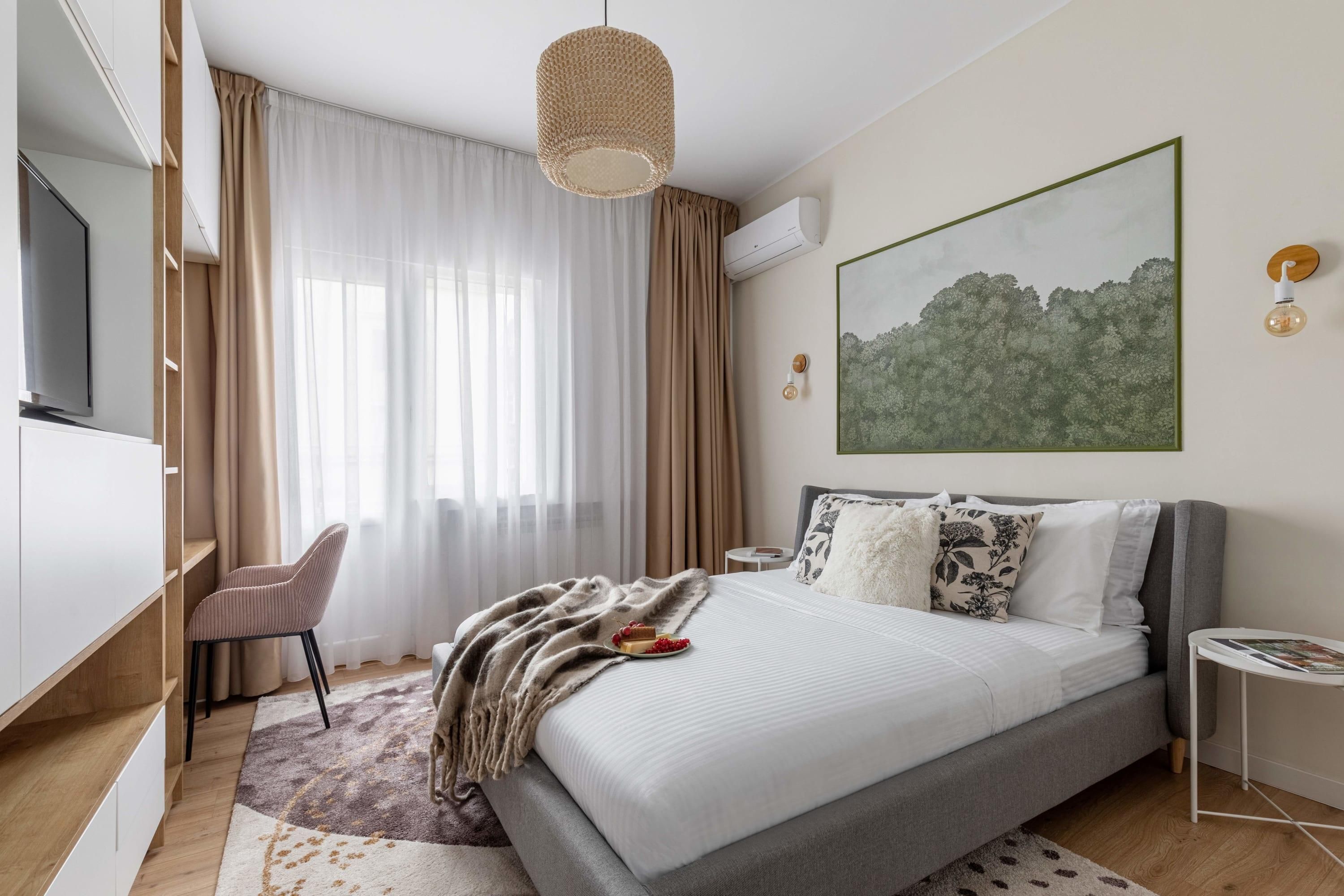 Un dormitori modern amb llit, escriptori, cadira i una finestra gran amb cortines.