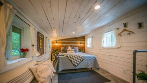 A cozy bedroom with a bed, a window, a bedside table, and a rug. - Cozy Cabin Little Red Hen 12 min to Magnolia (Waco)
