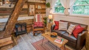 A rustic cabin interior with a wooden staircase, a cozy living area with a leather sofa, a wooden coffee table, and a fireplace. - Cozy Cabin Little Red Hen 12 min to Magnolia (Waco)