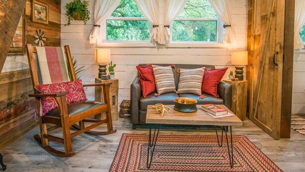 A cozy room with a wooden ceiling, a sofa with cushions, a rocking chair, a small table with a bowl, and a patterned rug. - Cozy Cabin Little Red Hen 12 min to Magnolia (Waco)