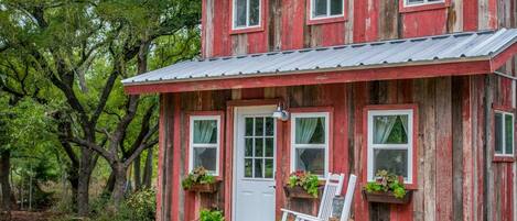 A rustic two-story house with a front porch, a white door, and multiple windows.