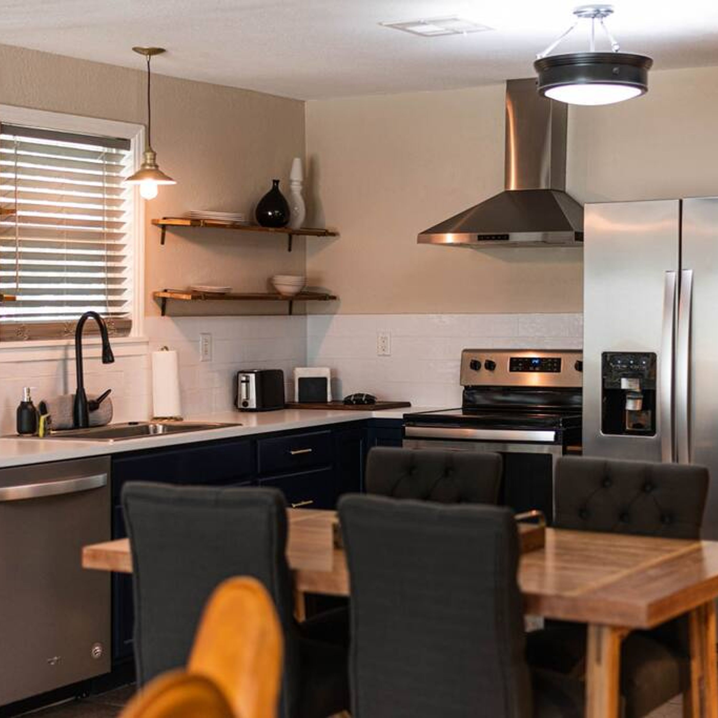 A modern kitchen with a dining area, featuring a stainless steel refrigerator, a built-in oven, and a gas stove.