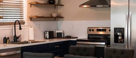 A modern kitchen with a dining area, featuring a stainless steel refrigerator, a built-in oven, and a gas stove.