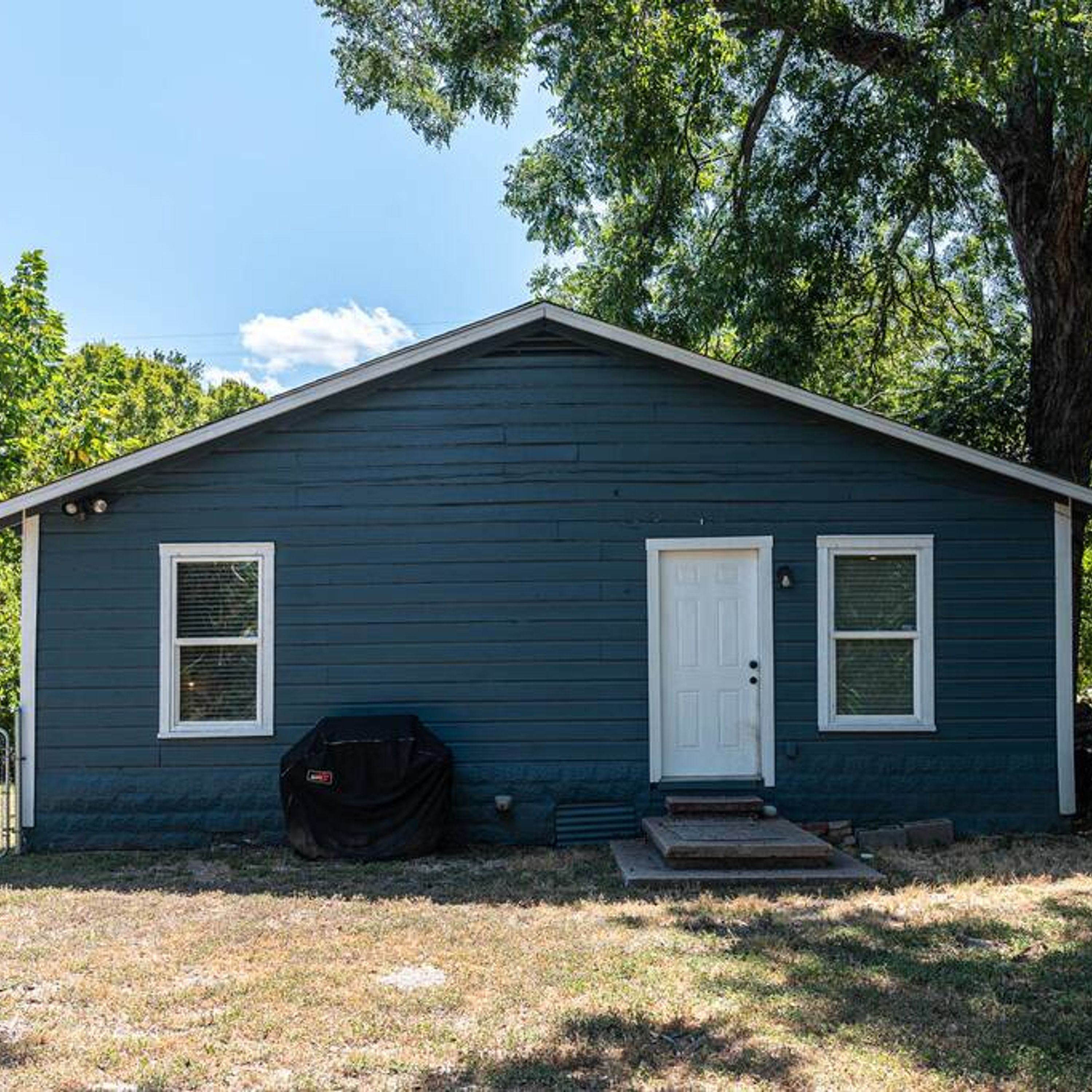 Une petite maison de plain-pied, à l’extérieur d’un bleu foncé, avec une porte blanche et deux fenêtres aux cadres blancs.