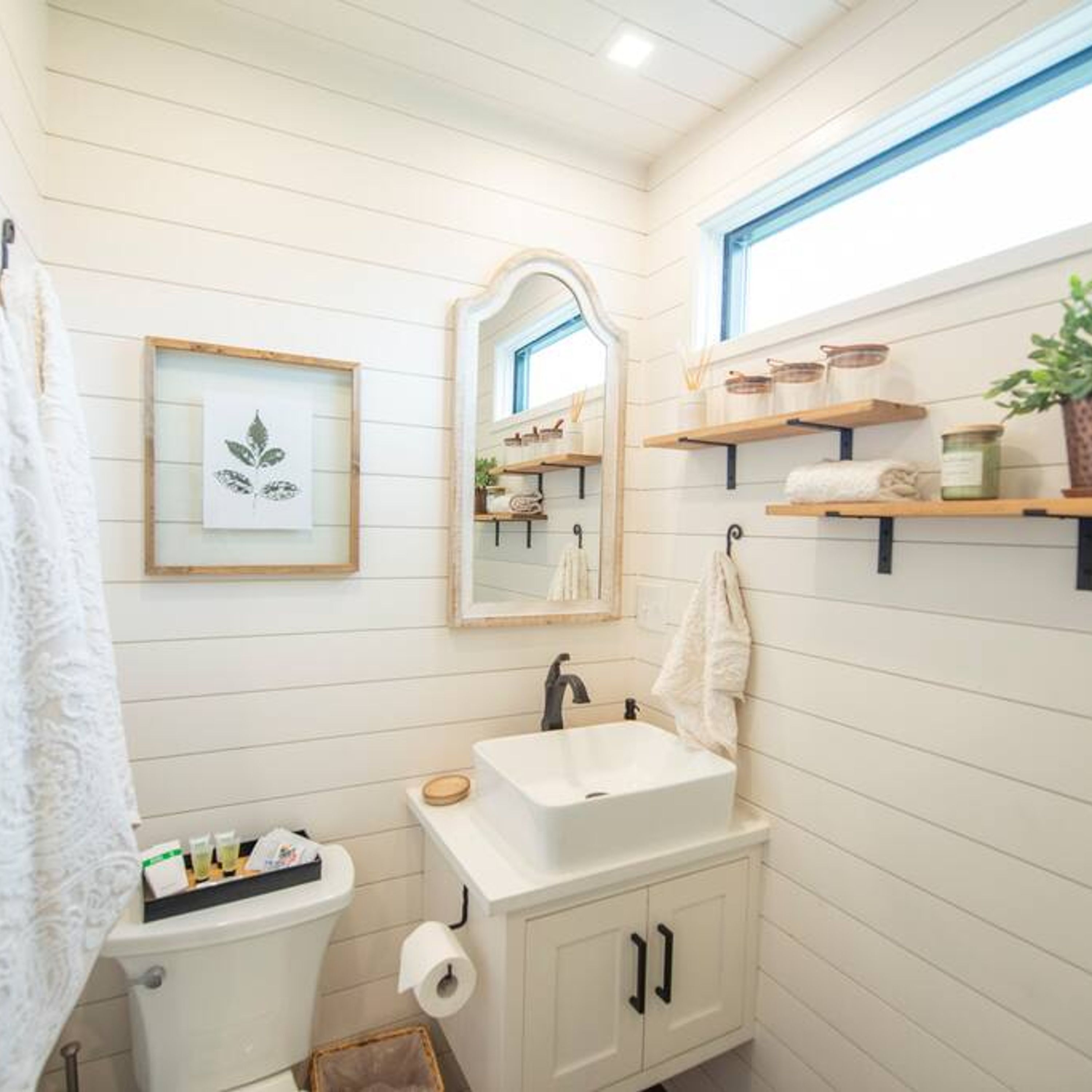 A bathroom with a white sink, toilet, and shelves with toiletries.