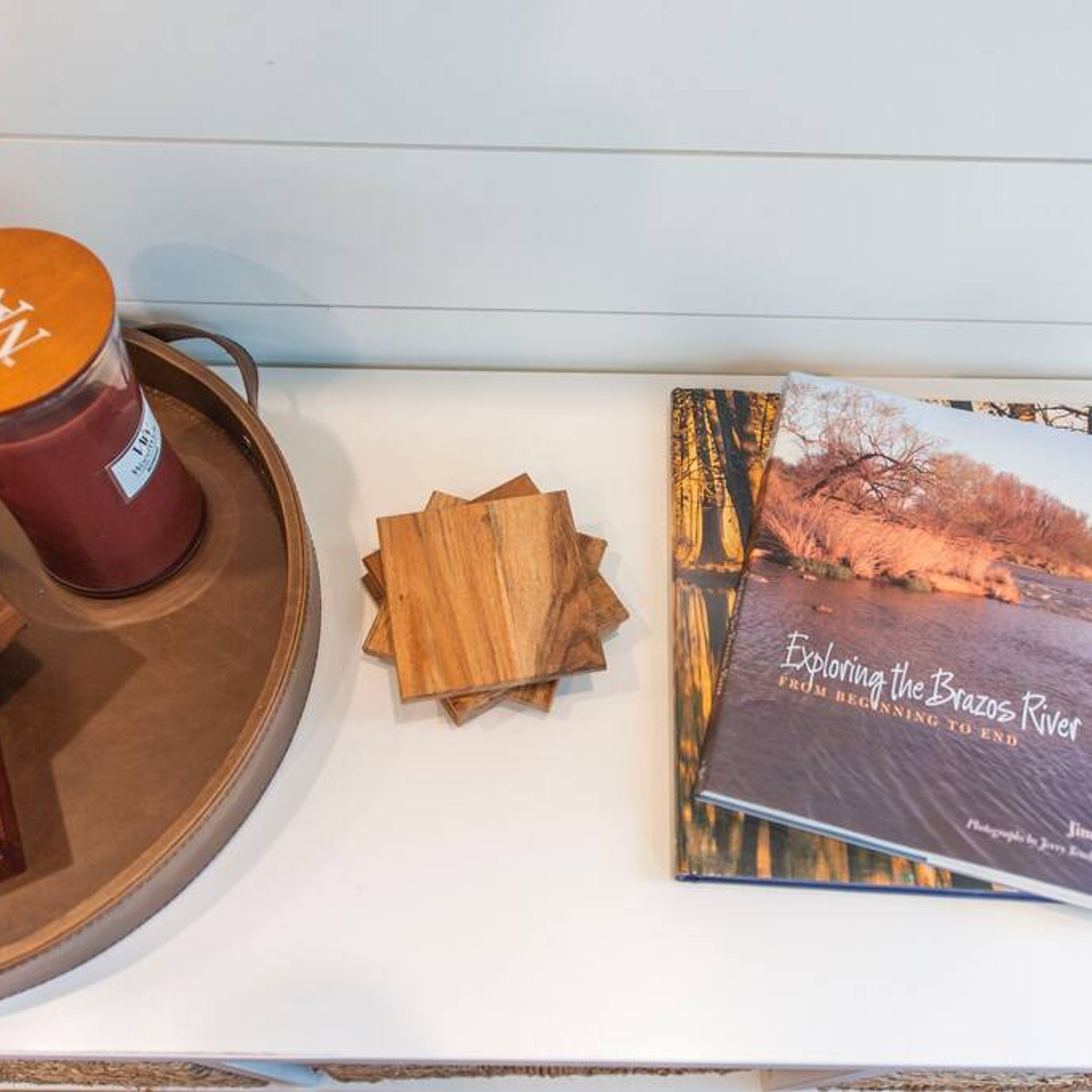 A book titled 'Exploring the Brazos River' and a wooden tray with a candle.