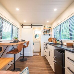 A compact kitchen with a dining area, wooden flooring, and large windows. - No Cleaning Fee Cozy Container Home The Brazos (Waco)
