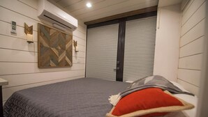 Ein Schlafzimmer mit einem Bett, einer Wand-Klimaanlage, einem Wandbild und einem Fenster mit Jalousien.