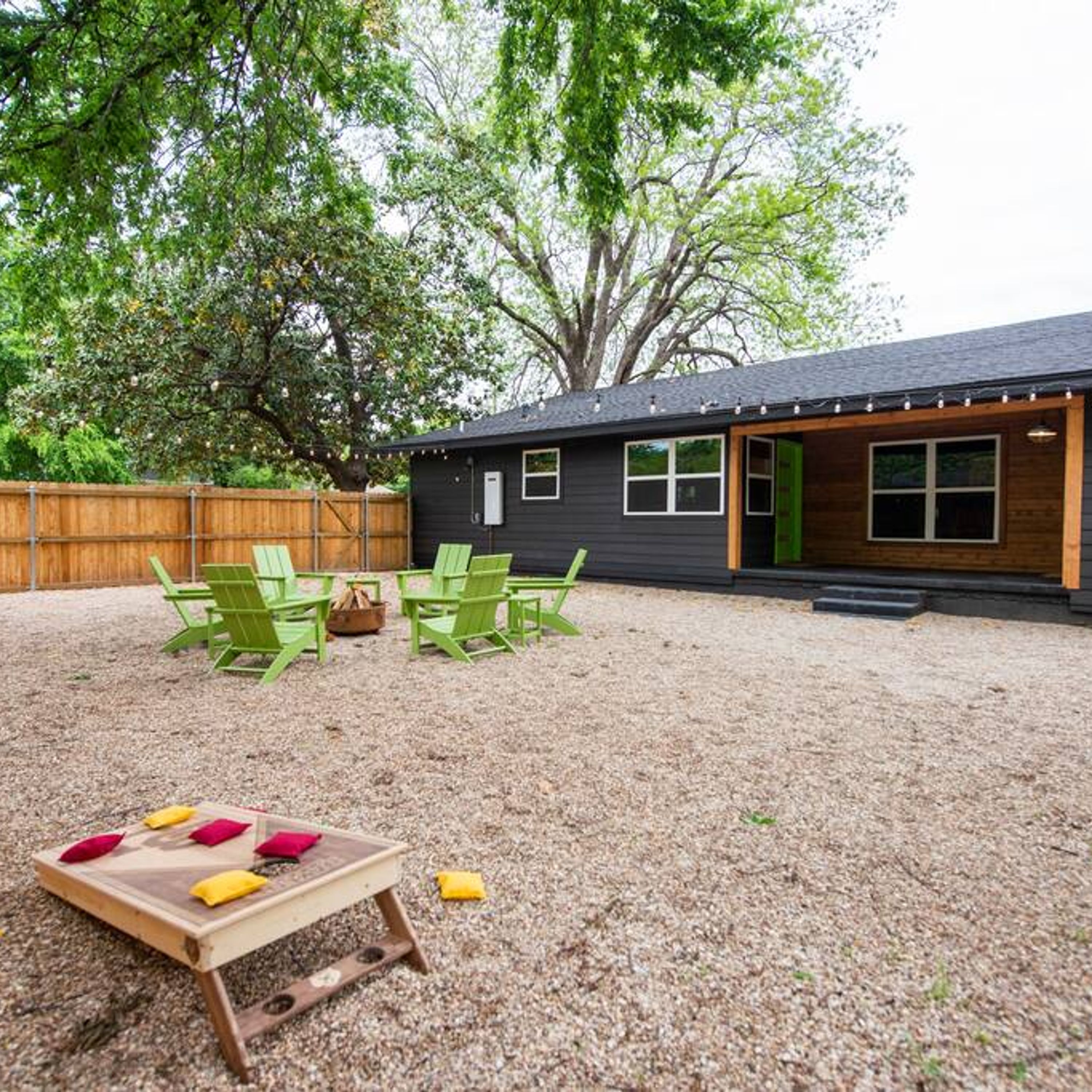 A backyard with a wooden deck, green chairs, and a small table with cushions.
