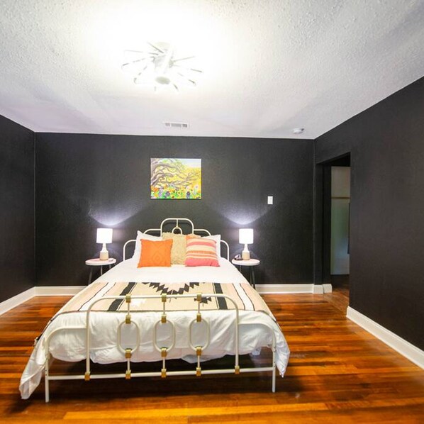 Un dormitorio con una cama, dos lámparas de noche, un cuadro en la pared y suelo de madera.