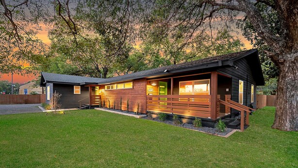 Ein modernes Blockhaus mit einer großen Terrasse, einer überdachten Veranda und einem gepflegten Rasen.