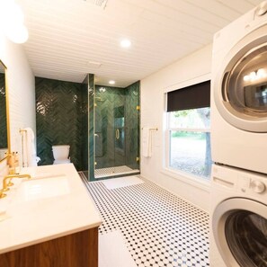 Een moderne badkamer met een douche met glazen wand, een groot wastafel en een wasmachine.