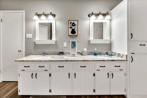Une salle de bain dotée d’un meuble-lavabo double, de deux miroirs fixés au mur et d’une œuvre d’art encadrée au-dessus du lavabo.