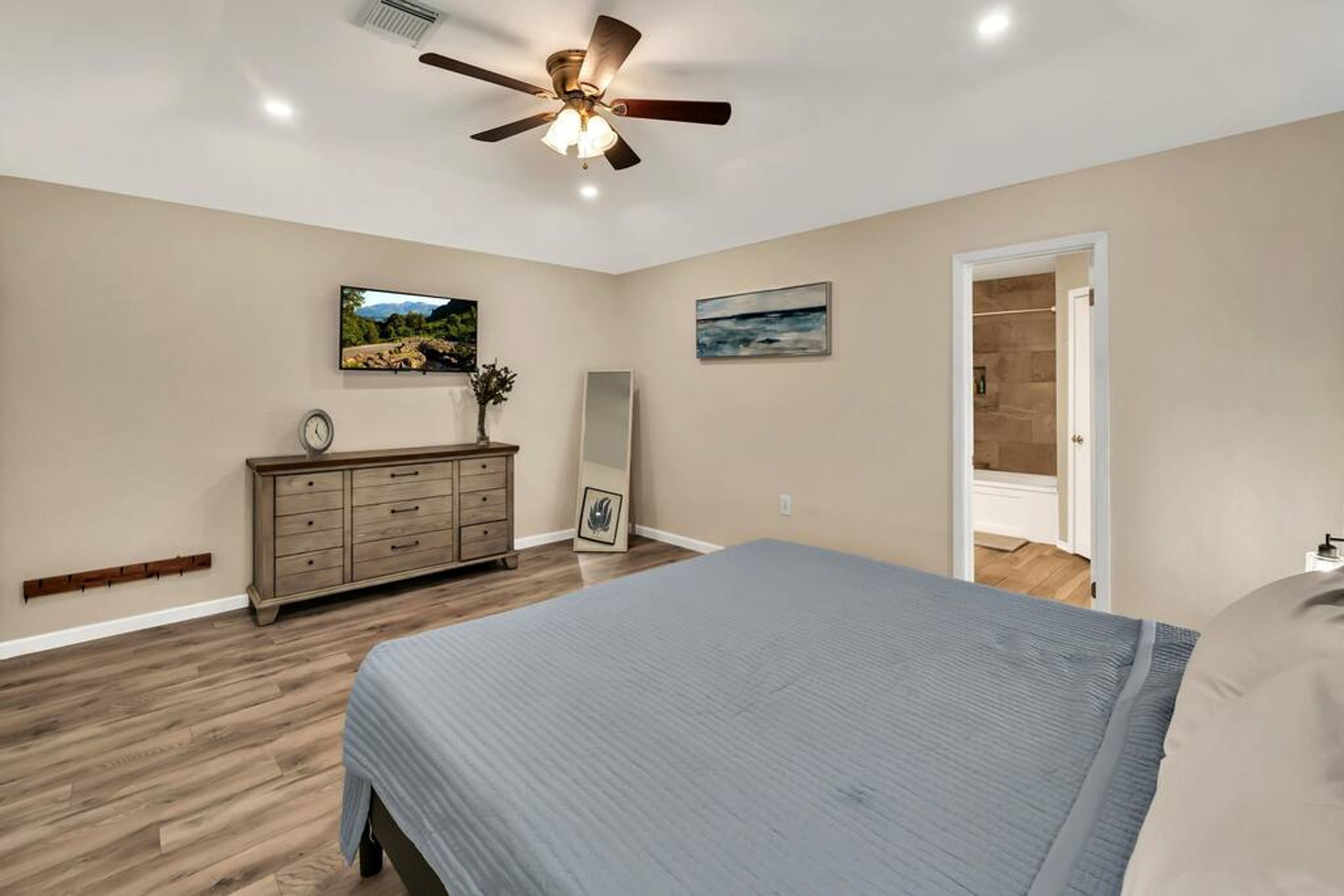 A bedroom with a bed, dresser, ceiling fan, and two paintings on the wall.
