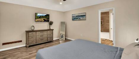 A bedroom with a bed, dresser, ceiling fan, and two paintings on the wall.