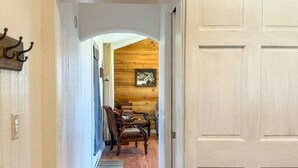 A hallway with wooden flooring, a white door, and a rustic interior with a wooden ceiling and a framed picture. - Wagon Wheel Cottage Couples Getaway in the Country (Waco)