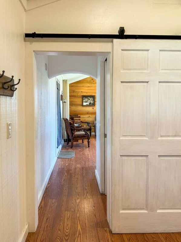 A hallway with wooden flooring, a white door, and a rustic interior with a wooden ceiling and a framed picture. - Wagon Wheel Cottage Couples Getaway in the Country (Waco)