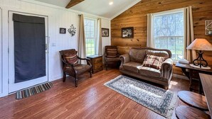 A cozy living room with wooden beams, a leather sofa, a wooden coffee table, and a rug. - Wagon Wheel Cottage Couples Getaway in the Country (Waco)