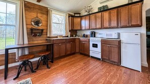 A kitchen with wooden cabinets, a countertop, a stove, a microwave, and a refrigerator. - Wagon Wheel Cottage Couples Getaway in the Country (Waco)