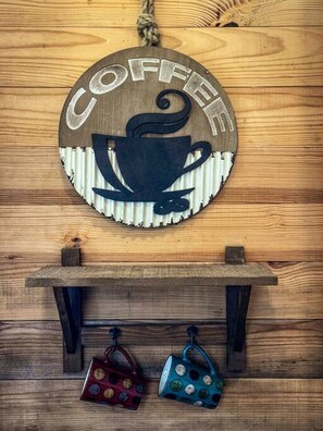 En vägg av trä med en rund skylt som visar ordet "KAFFE" och en illustration av en kaffekopp. Under skylten finns en hylla med två muggar.