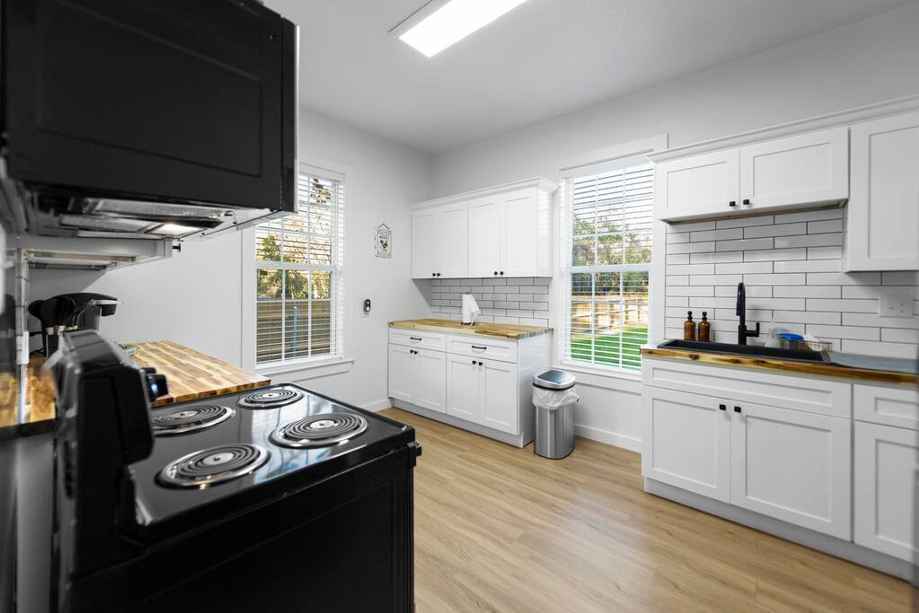 A kitchen with white cabinets, a black stove, and a window with blinds.
