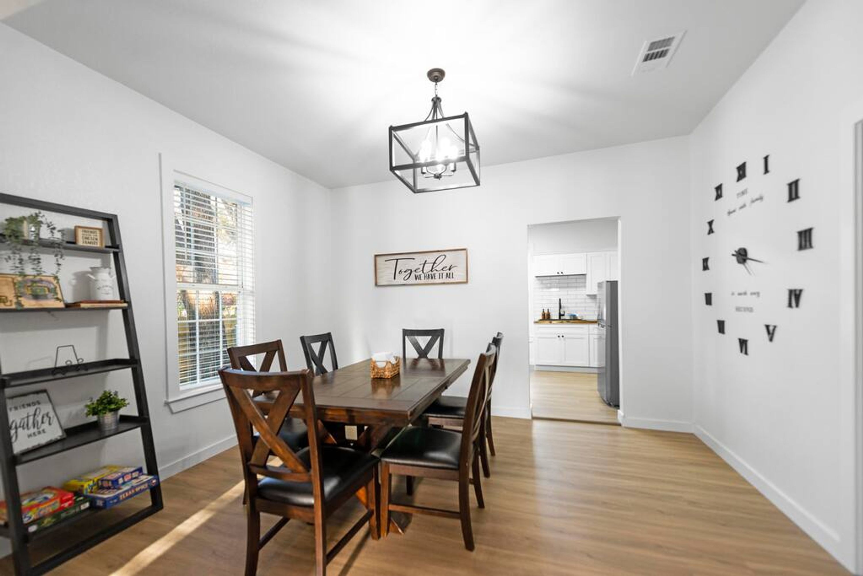 A dining area with a wooden table and chairs, a chandelier, and a wall with clock numbers.