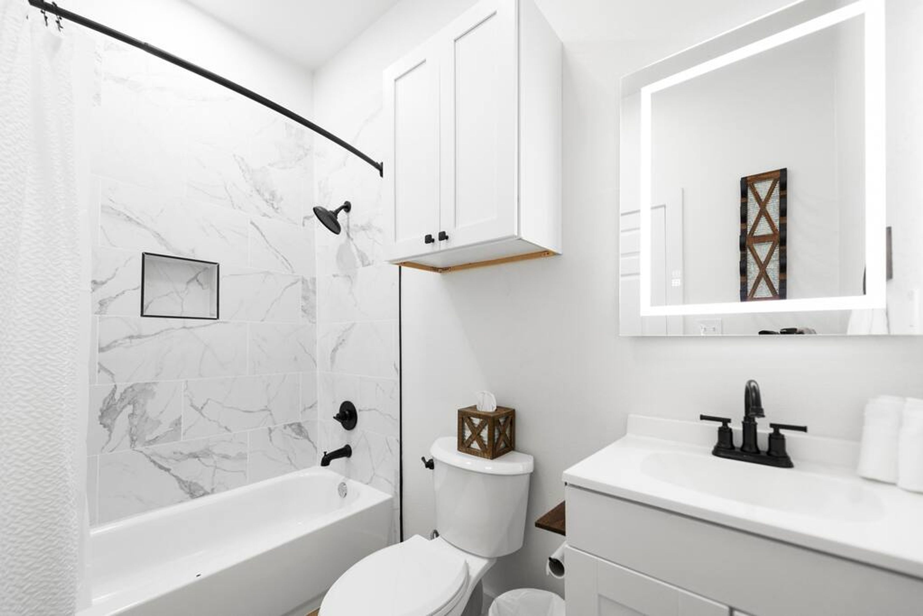 Un bagno moderno con parete doccia in marmo, un water bianco, una vasca da bagno, un lavandino con rubinetto nero e uno specchio sopra il lavandino.