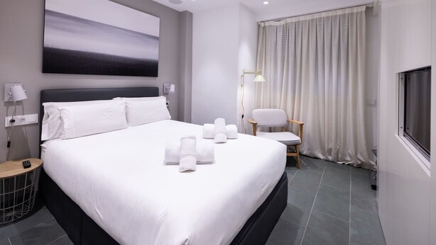 Een moderne hotelkamer met een groot bed, een flatscreen televisie, een schilderij aan de muur en een raam met gordijnen.