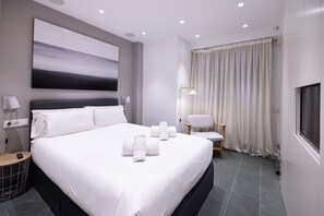 Una habitación de hotel moderna con una cama grande, un televisor de pantalla plana, un cuadro en la pared y una ventana con cortinas.