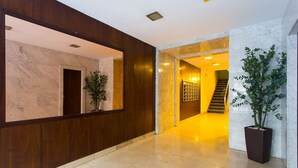 Een moderne lobby met een marmeren muur, houten lambrisering en een trap naar een hoger niveau.