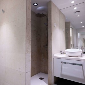 Un baño moderno con cabina de ducha, un espejo grande y un lavabo blanco.