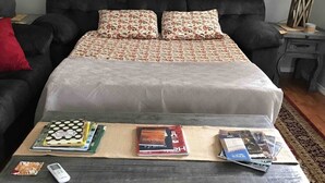 Ein Schlafzimmer mit einem Bett, einer hölzernen Kommode und einem kleinen Tisch mit Büchern und einer Fernbedienung.