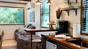 A modern kitchen with wooden beams, a dining area with a bench, and a living room with a sofa and decorative items. - The Shoreline Container Tiny Home 12 min to Magnolia Baylor (Waco)