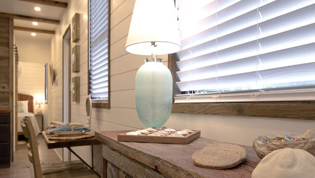 A wooden reception desk with a lamp, a remote control, and decorative items. - The Shoreline Container Tiny Home 12 min to Magnolia Baylor (Waco)