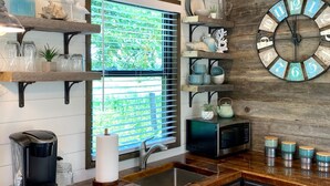 A kitchen with wooden shelves, a clock, and a window with blinds. - The Shoreline Container Tiny Home 12 min to Magnolia Baylor (Waco)