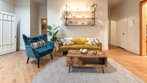 A living room with a blue armchair, a mustard sofa, and a wooden coffee table. There are shelves above the sofa and a door to the left. - New Gathering Place on Columbus (Waco)