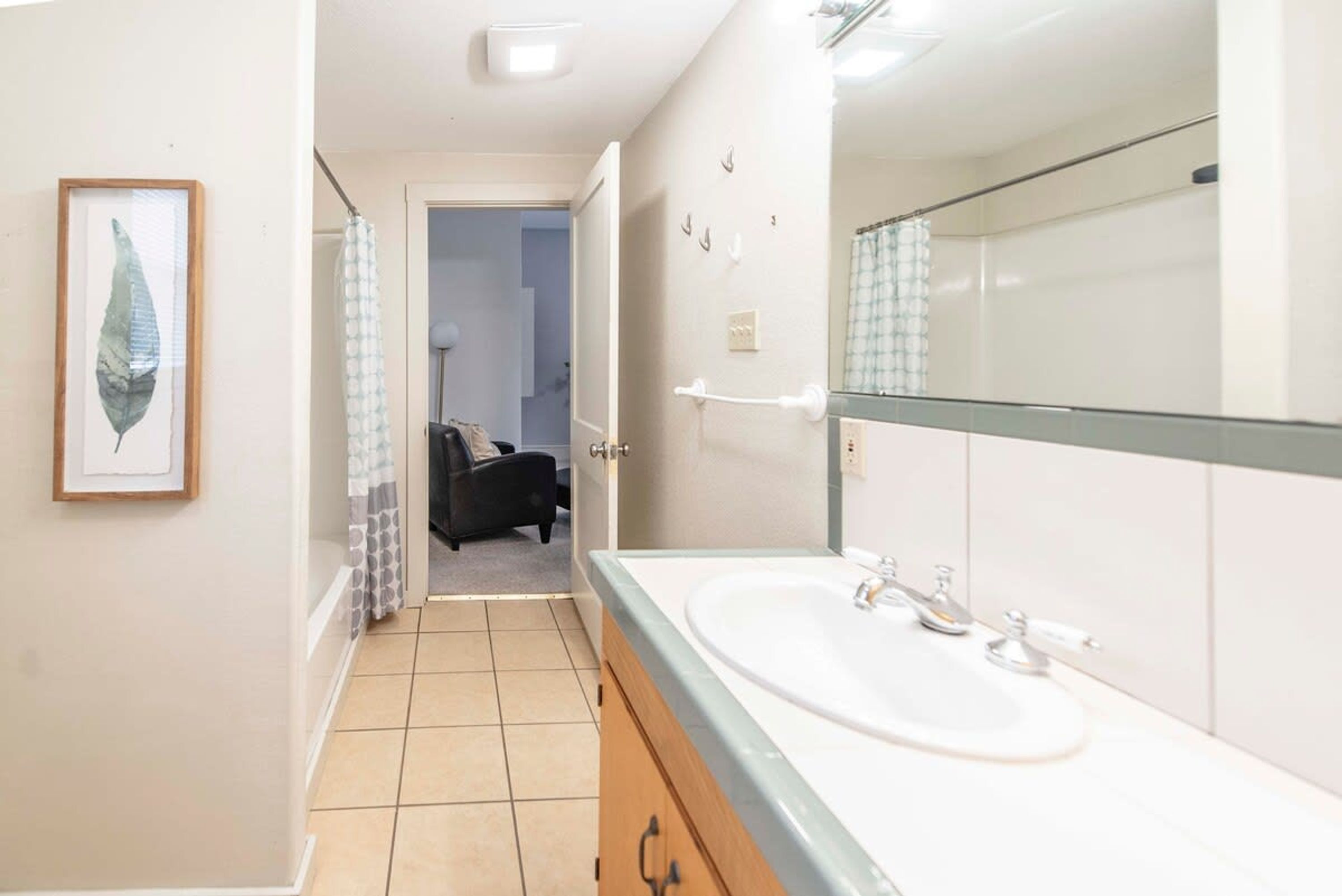 Une salle de bain avec un grand miroir, un lavabo et une œuvre d’art représentant une feuille, encadrée et accrochée au mur.