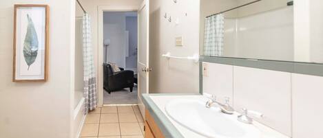 Une salle de bain avec un grand miroir, un lavabo et une œuvre d’art représentant une feuille, encadrée et accrochée au mur.