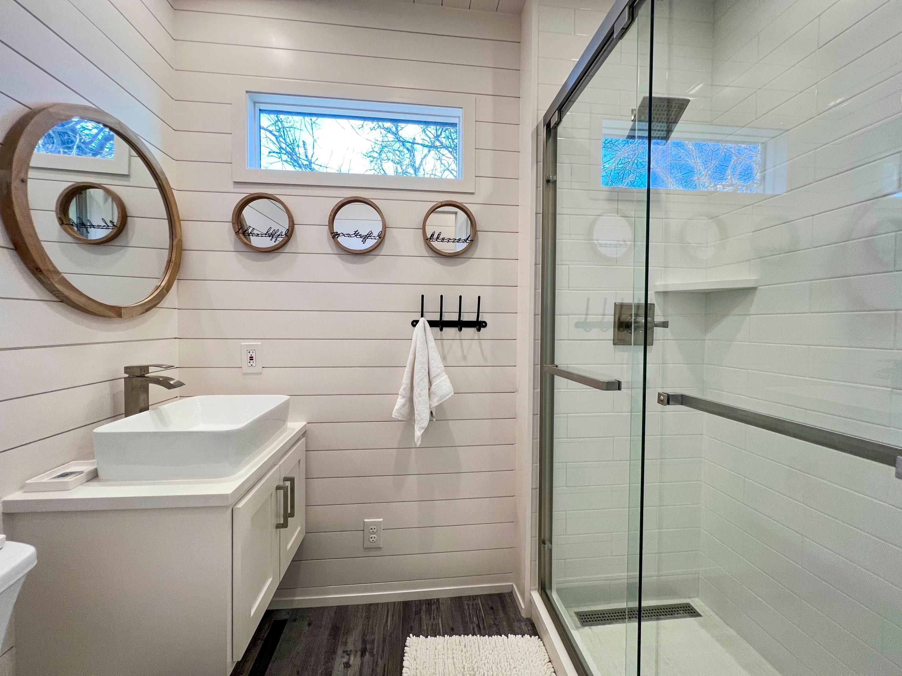 A modern bathroom with a white sink, vanity, and a glass shower enclosure.
