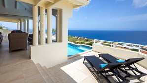 A balcony with a pool, lounge chairs, and a view of the ocean. - Shoreline Harmony at Villa Solana (Sint Willibrordus)