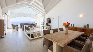 A spacious living area with a wooden dining table, wicker chairs, and a view of the ocean. - Shoreline Harmony at Villa Solana (Sint Willibrordus)