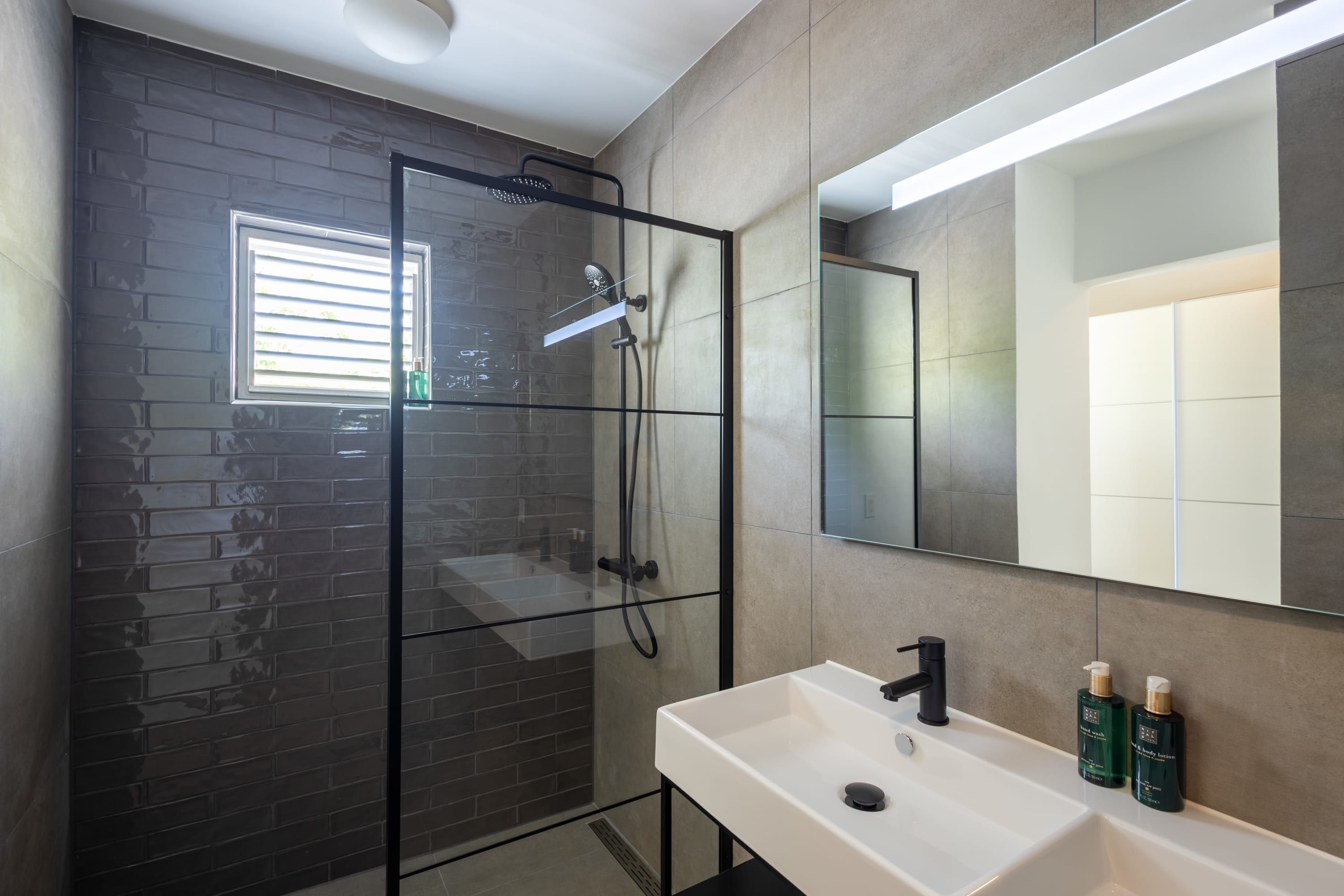 A modern bathroom with a glass-enclosed shower, a white sink, and a large mirror.