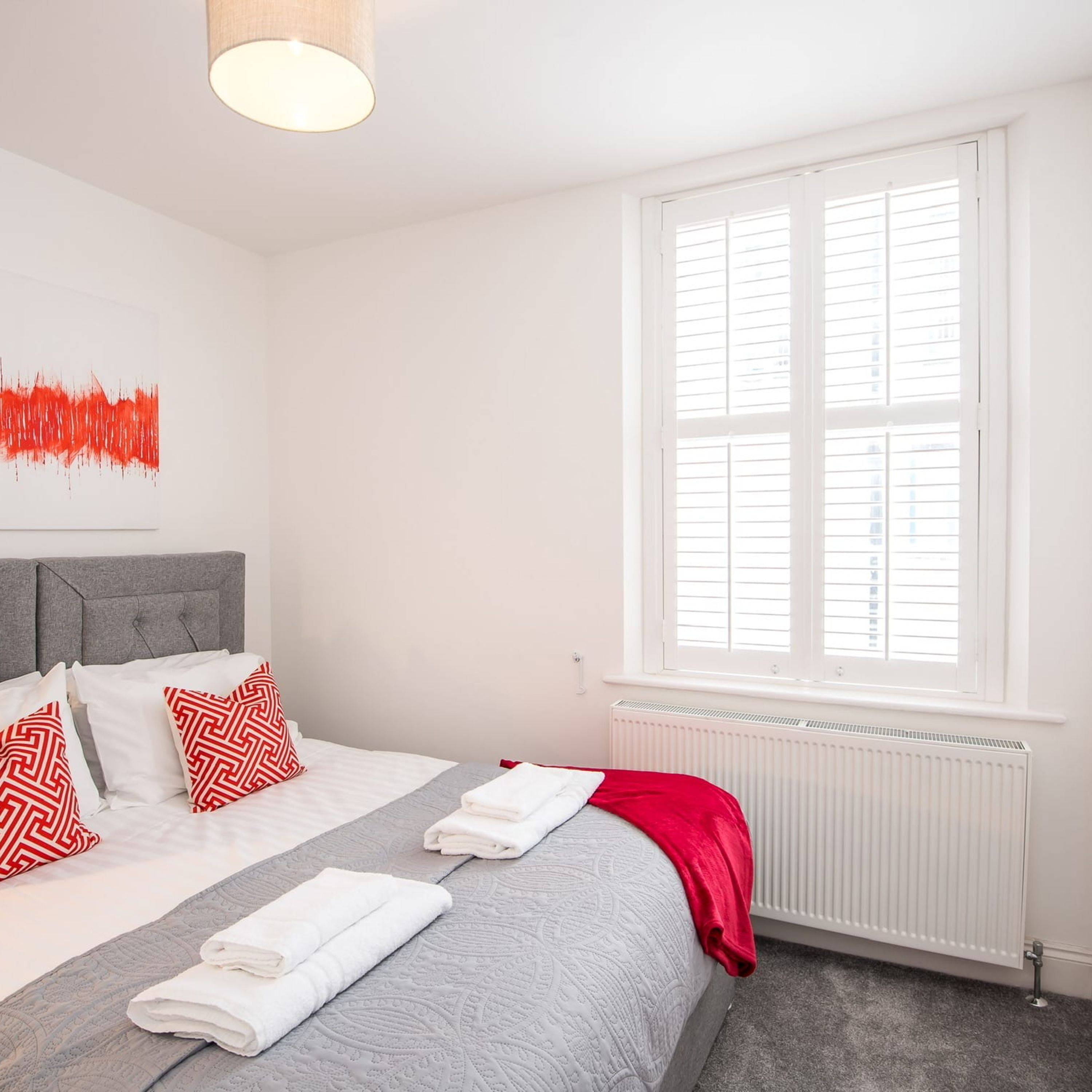 A modern bedroom with a large bed, a radiator, and a window with blinds.