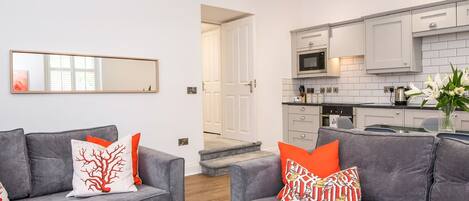 A modern living room with two grey sofas, a glass coffee table, and a large mirror on the wall.