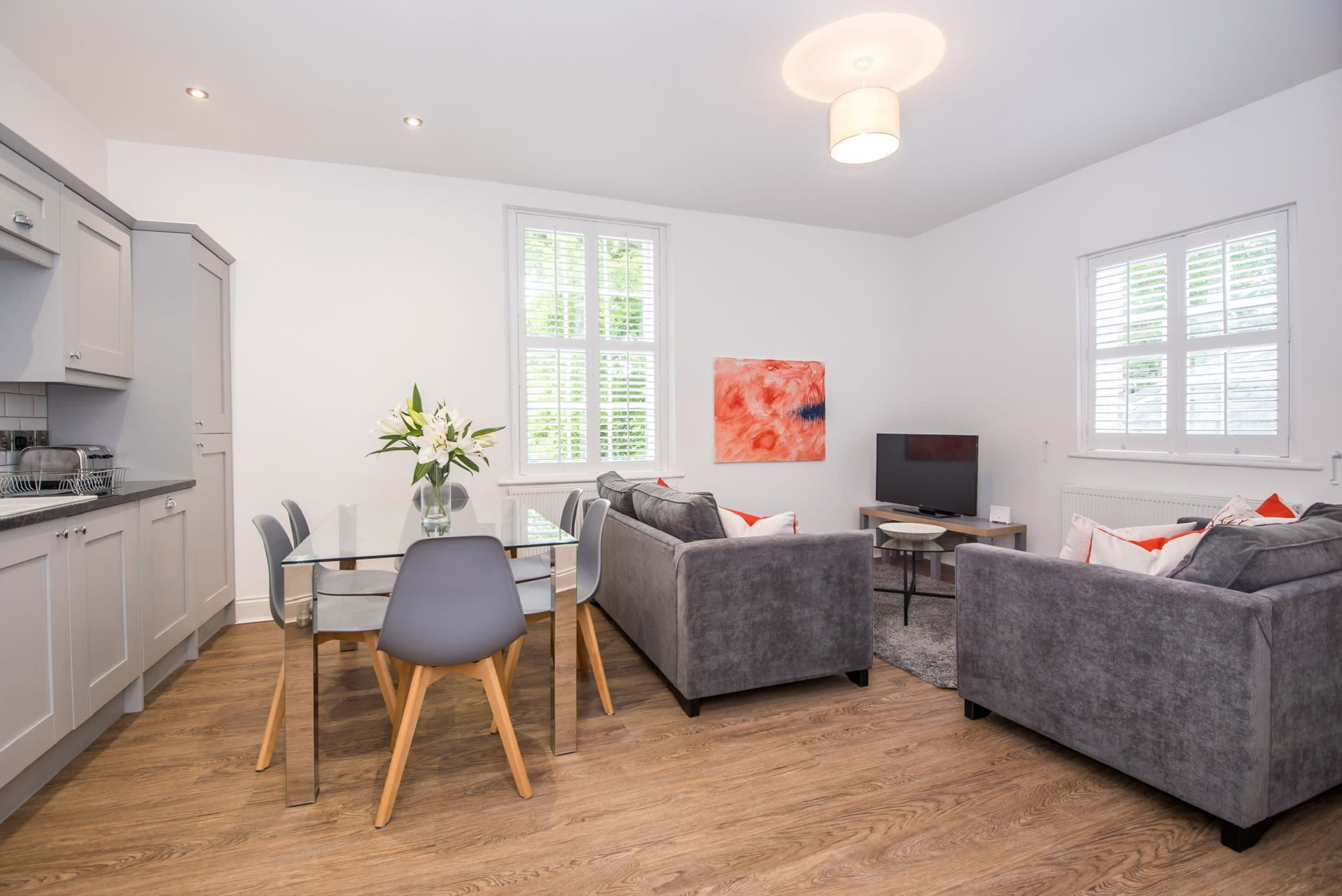 A modern living room with grey sofas, a glass dining table, and a TV.