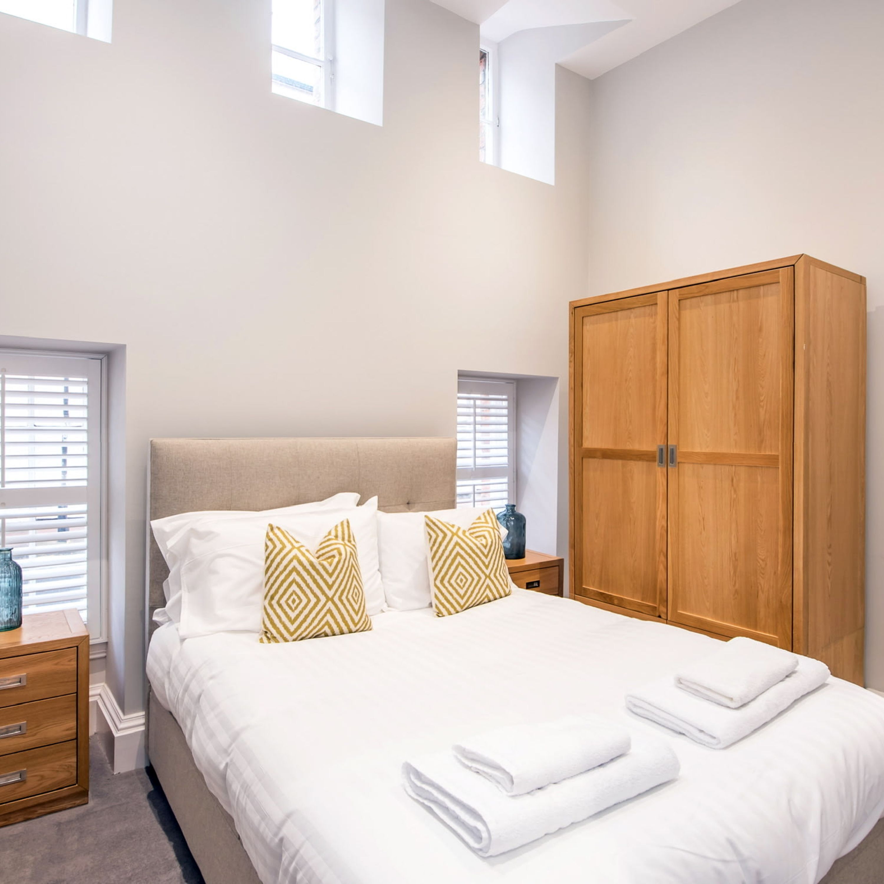 A bedroom with a bed, two nightstands, a wardrobe, and windows with blinds.