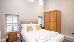 A bedroom with a bed, wooden wardrobe, bedside tables, and windows. - The Barrington (Durham)