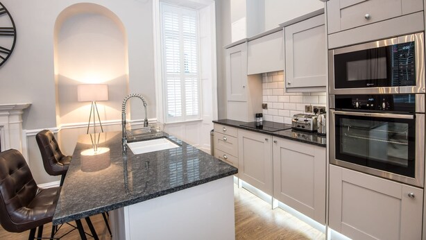 A modern kitchen with a granite countertop, stainless steel appliances, and a dining area with leather chairs. - The Barrington (Durham)
