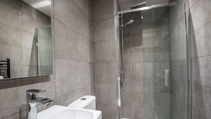 A modern bathroom with a glass-enclosed shower, a white sink, and a toilet. - The Barrington (Durham)
